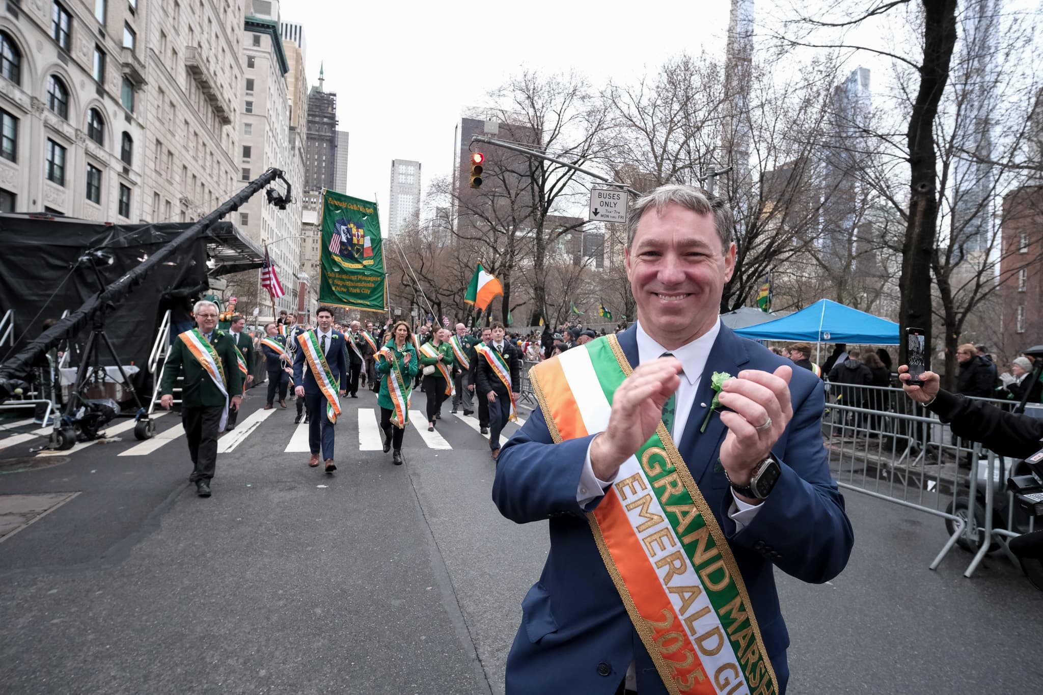 2025 Emerald Guild Society Grand Marshal applauding along the parade route while the Guild procession follows behind.
