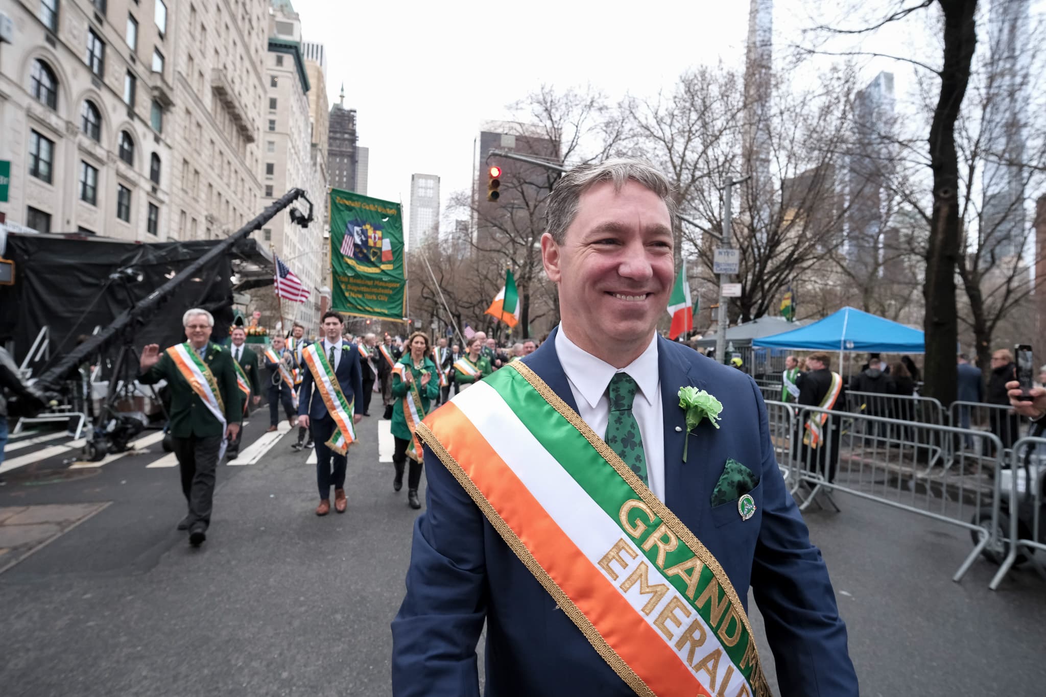 2025 Emerald Guild Society Grand Marshal walking the parade route with the Guild banner visible behind him.
